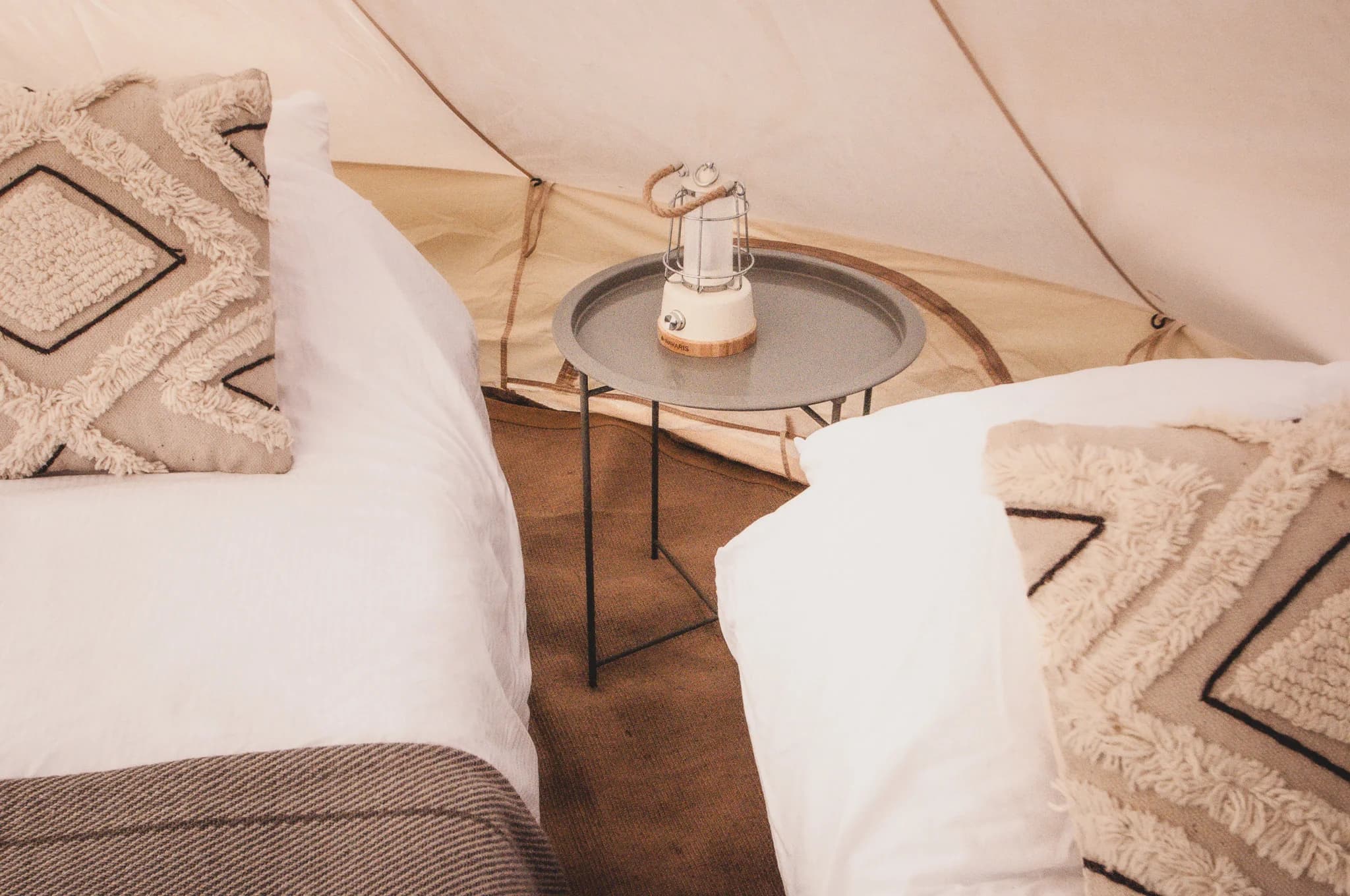 A lit lantern on a round tray table between two beds inside a Hotel Melody Lyrical Lounge bell tent.