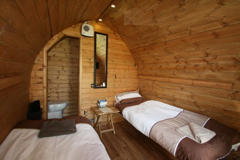 Two single beds inside a wooden camping pod at Hotel Melody's Private Lodge, with an en-suite door and mirror.