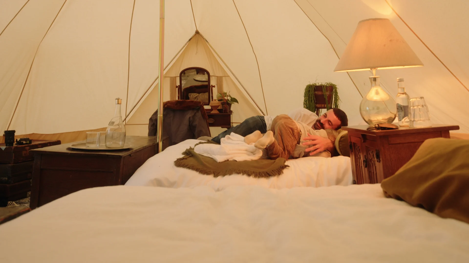 A guest relaxes on the bed inside a Hotel Melody Rhythm Resort tent, beside a dressing table and drinks tray.