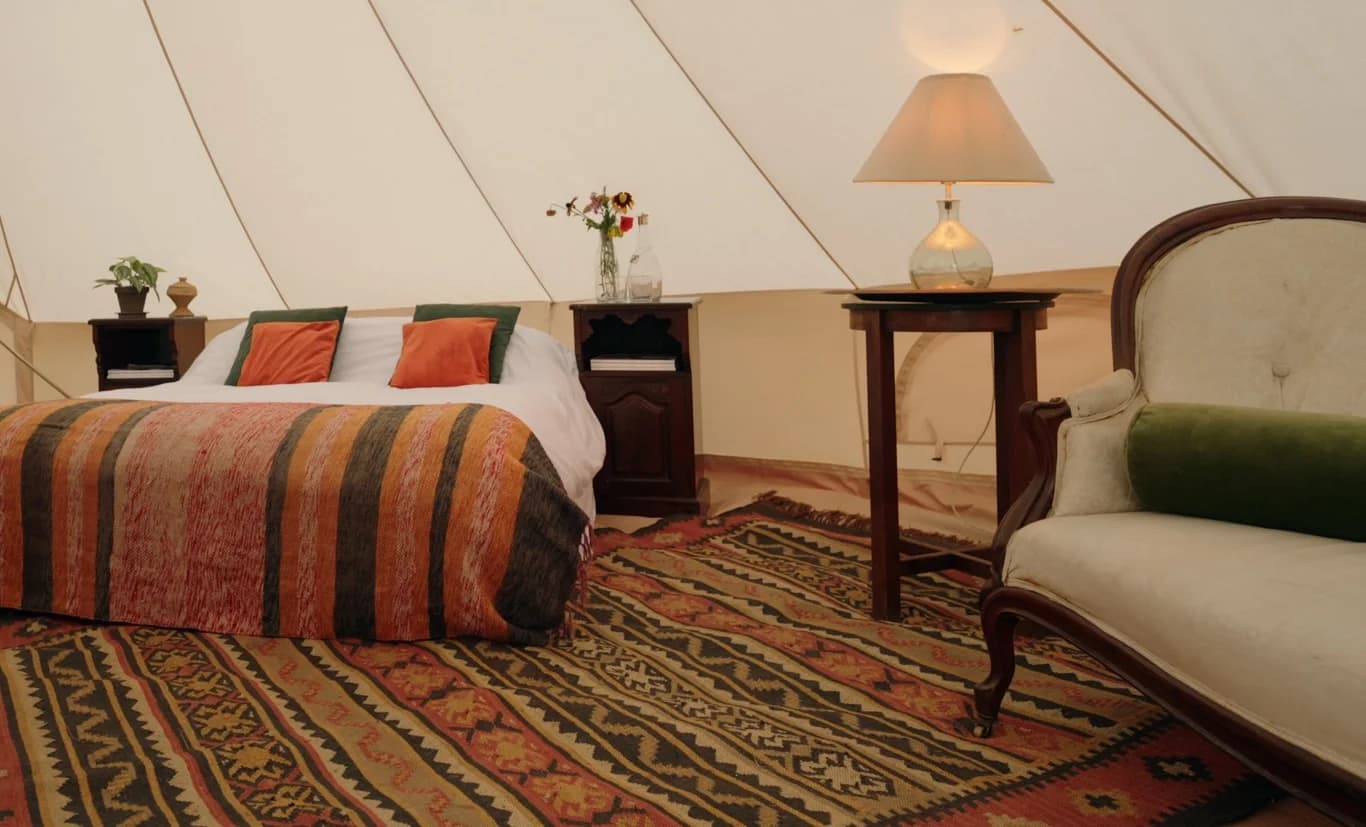 A bed with a striped orange and black blanket inside a Hotel Melody Rhythm Resort tent, beside a cream armchair and side table.